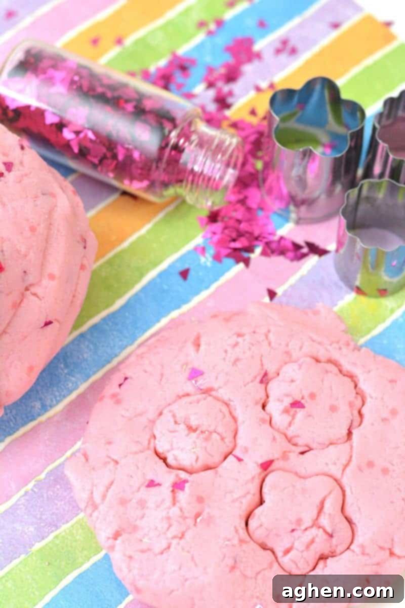 A child's hands playing with the homemade glittery pink princess playdough, showcasing its soft and pliable texture. This easy no-cook recipe is perfect for creative and sensory play, made with simple ingredients like cake mix, icing, olive oil, and glitter.