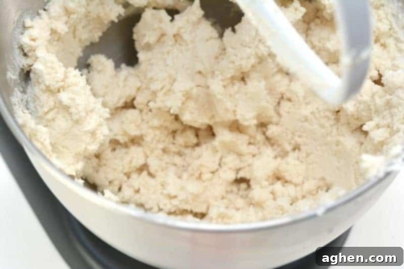 A mixer combining white cake mix and white whipped frosting to form a crumbly mixture, the first step in making no-cook pink princess playdough. This easy recipe uses simple ingredients for a fun sensory activity.