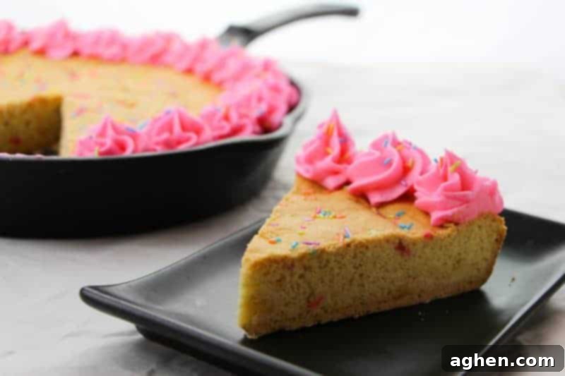 A beautifully decorated giant cast iron skillet cookie adorned with a generous layer of rainbow sprinkles and perfectly piped swirls of homemade pink frosting. The vibrant, funfetti design makes it an ideal dessert for festive celebrations.