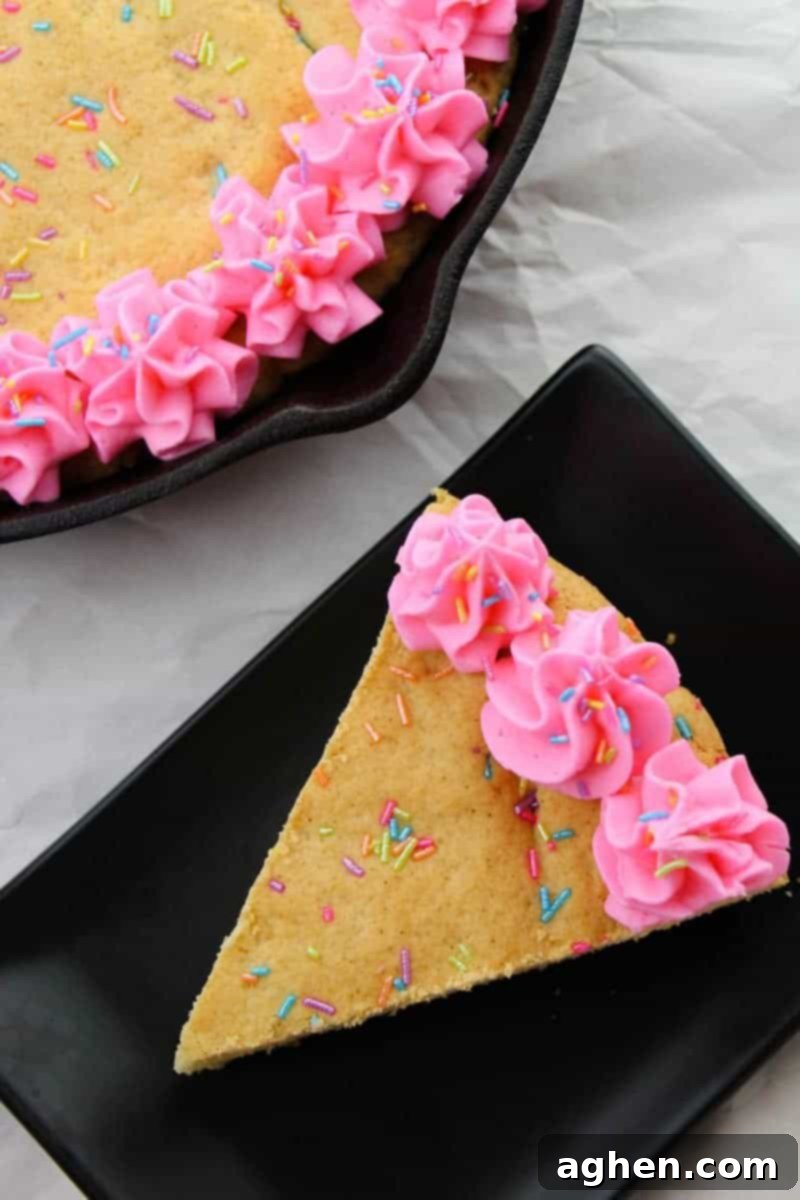 A golden-brown giant sugar cookie baked evenly in a cast iron skillet, with a scattering of rainbow sprinkles visible on its surface, waiting to be frosted and enjoyed.
