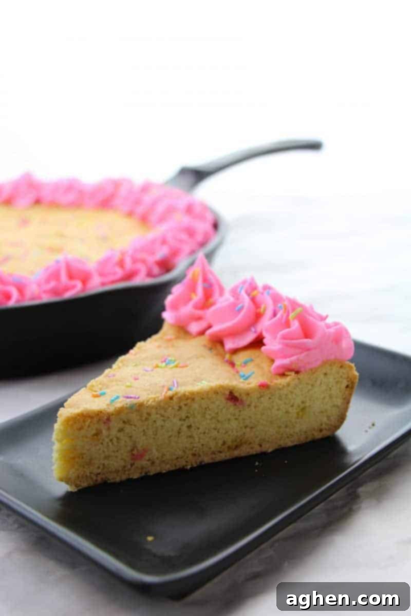 An overhead shot of the un-frosted gigantic sugar cookie baked perfectly golden-brown in a cast iron skillet, ready for its pink frosting and sprinkle toppings. The surface shows an even bake and tempting texture.