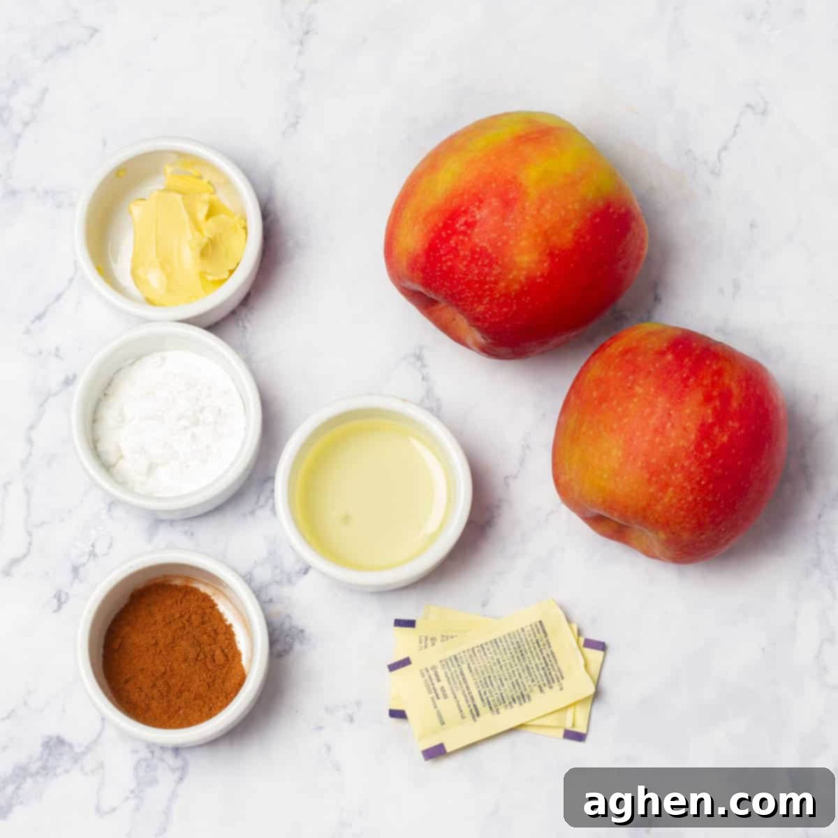 Ingredients of fresh apples, cinnamon, butter, and spices in separate dishes, ready for preparation.