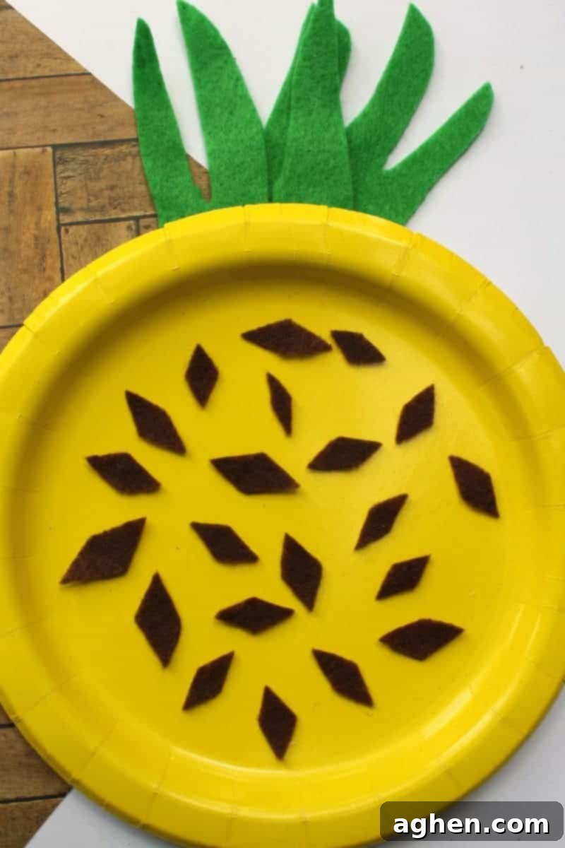 Smiling child proudly displaying their finished yellow paper plate pineapple craft, decorated with brown felt diamonds and green felt leaves, perfect for an easy summer kids activity.