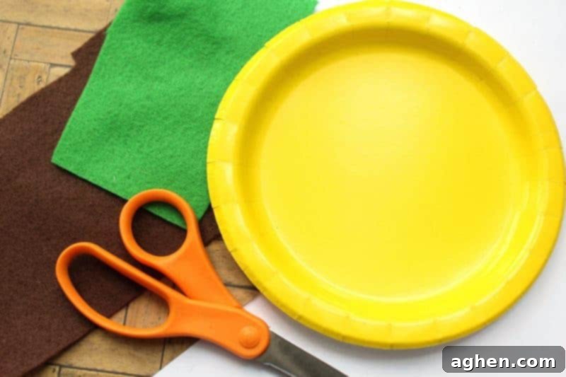 Close-up of craft supplies for the paper plate pineapple: brown and green felt, scissors, a yellow paper plate, and craft glue laid out on a wooden surface.