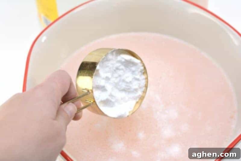 Baking soda being slowly sprinkled into the fabric softener mixture to prevent overflowing due to the chemical reaction.