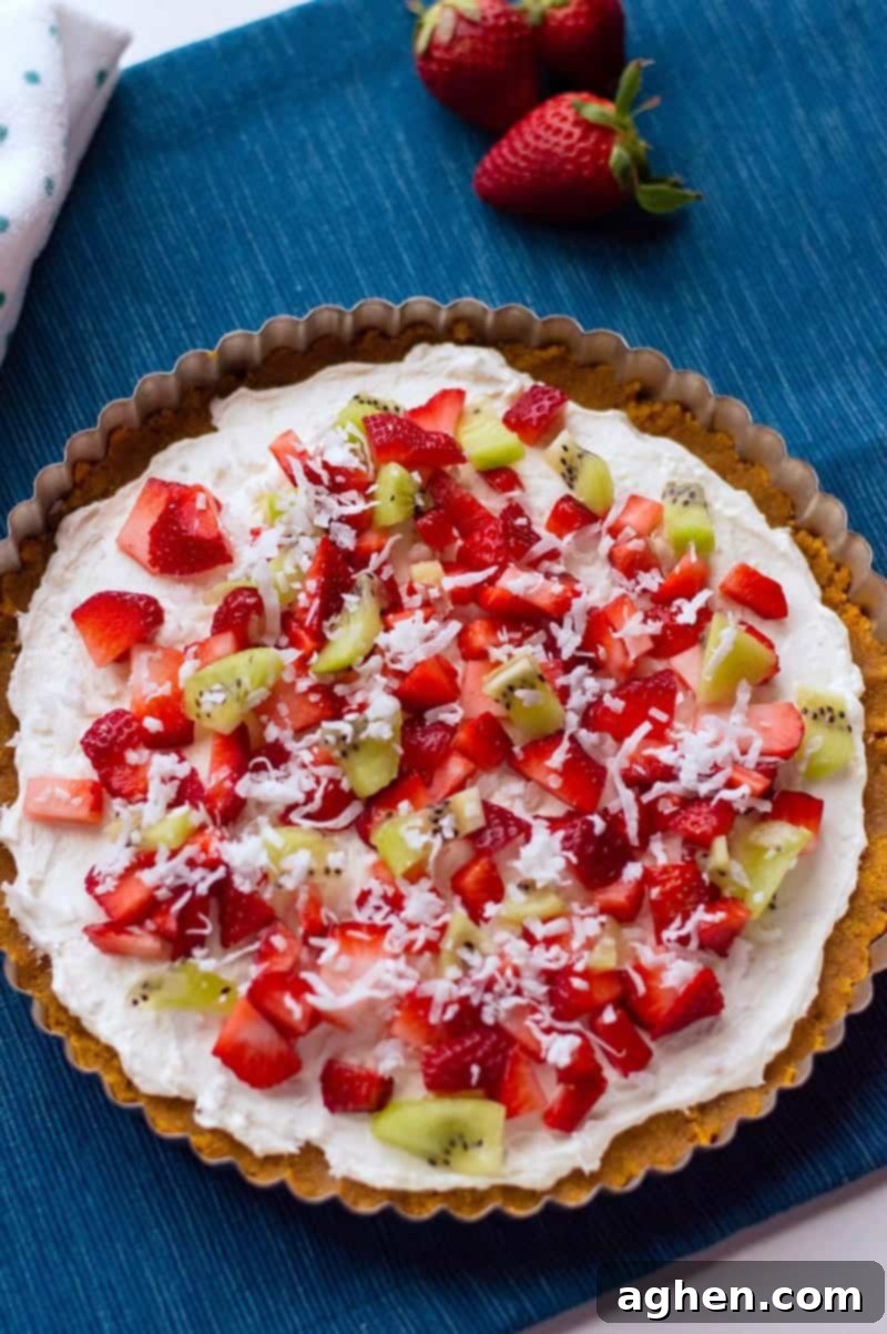 Close-up of a colorful dessert pizza with cream cheese and various fruit toppings on a graham cracker crust.