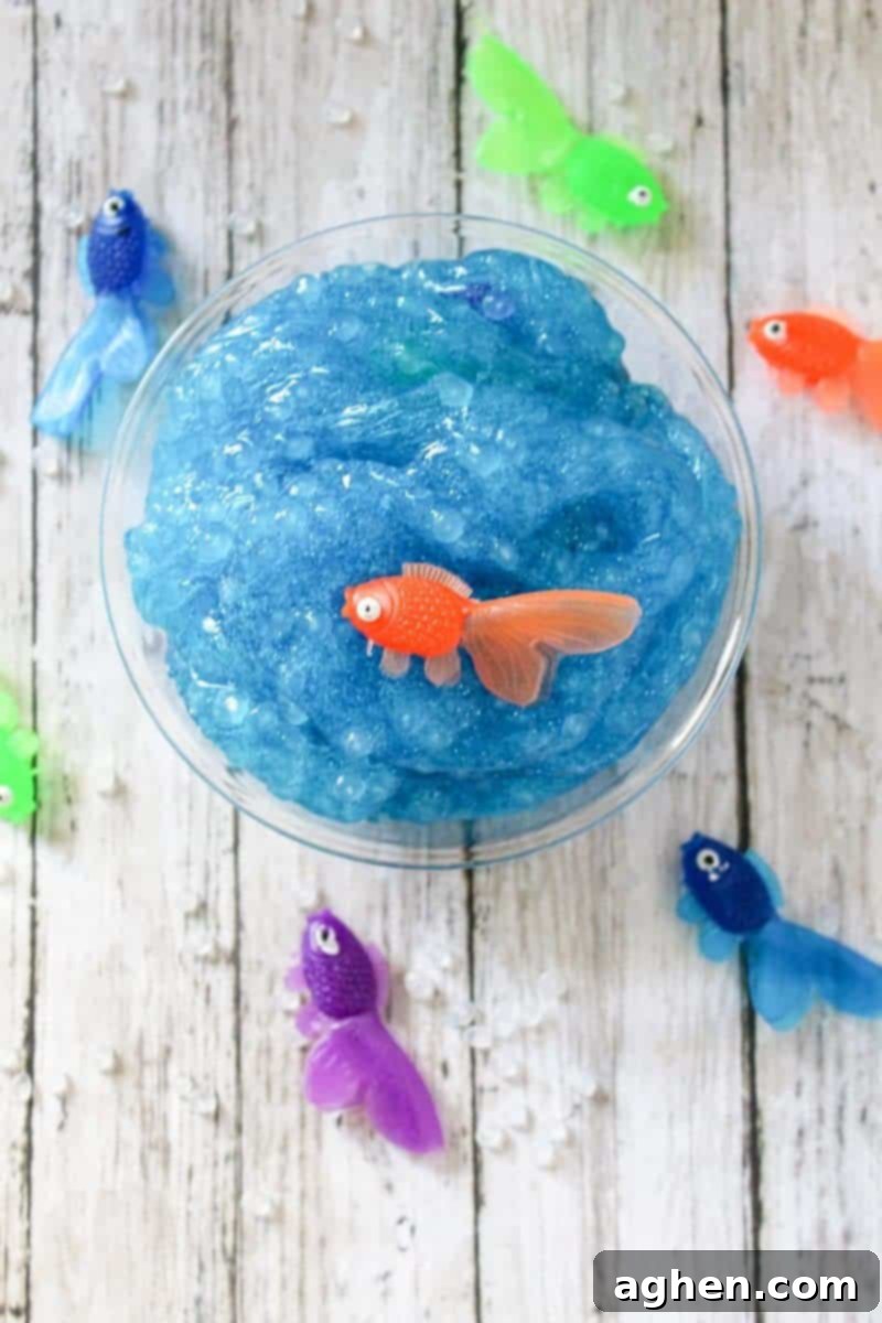 A close-up of vibrant blue, glittery, borax-free ocean slime, showcasing its texture and sparkle, with tiny plastic fish embedded, perfect for a summer sensory activity.
