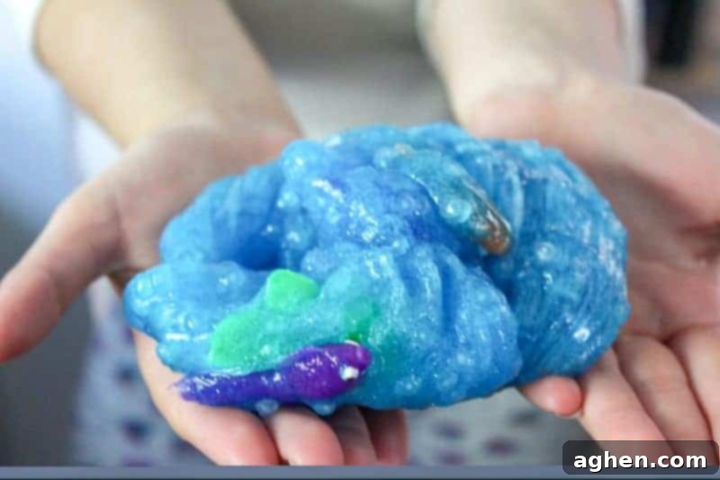 Close-up of sparkling blue borax-free ocean slime with several plastic fish embedded, demonstrating the slime's thick texture holding the toys for interactive play.