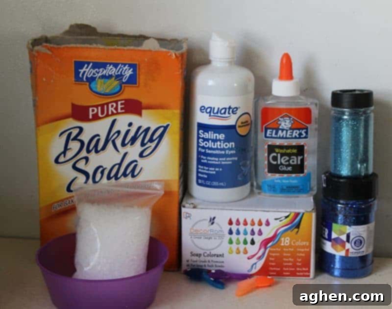 A flat lay photograph displaying all the essential ingredients and supplies for making borax-free ocean slime, including clear glue, baking soda, saline solution, soap colorant, blue glitter, clear fishbowl beads, and small plastic fish.