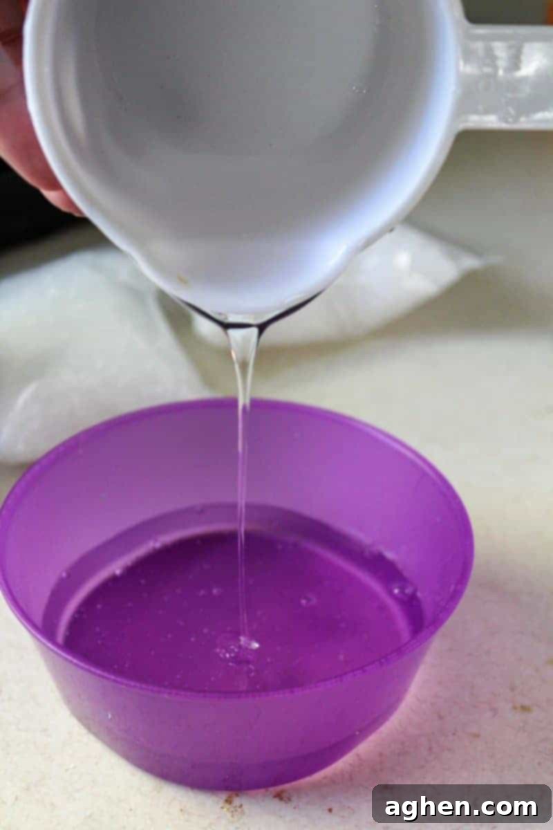 A hand pouring a full bottle of clear glue into a small mixing bowl, the initial step in the borax-free ocean slime recipe.