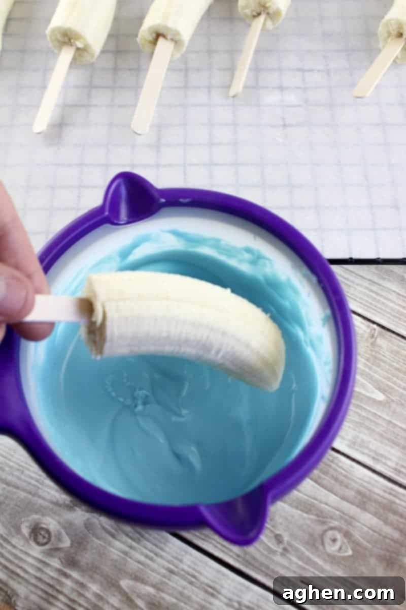 Child's hand dipping a banana half on a popsicle stick into a bowl of melted blue candy.