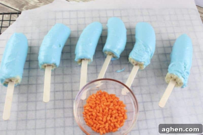 Blue candy-coated banana pops placed on parchment paper, ready for sprinkles.