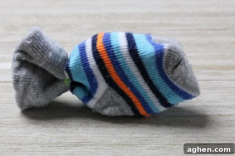 A baby sock partially filled with crumpled paper, demonstrating the stuffing process for a homemade cat toy.