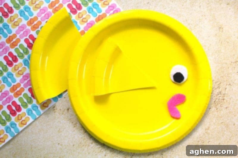 DIY Paper Plate Fish 2 A bright and colorful finished paper plate fish craft with a yellow body, pink lips, and a large eye, set against a light blue background.