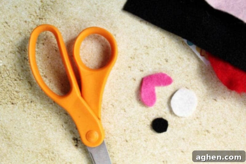 DIY Paper Plate Fish 5 Close-up of small felt pieces, including a pink crescent for lips, a large white circle for the eye, and a smaller black circle for the pupil, ready for assembly.