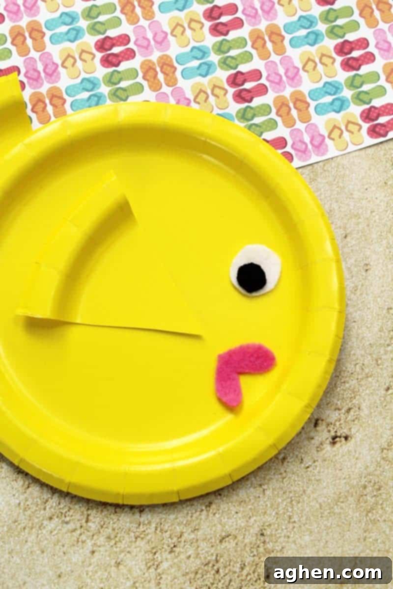 DIY Paper Plate Fish 7 A finished paper plate fish craft with its yellow body, pink lips, and a large eye, showcasing the attached side and tail fins, drying on a surface.