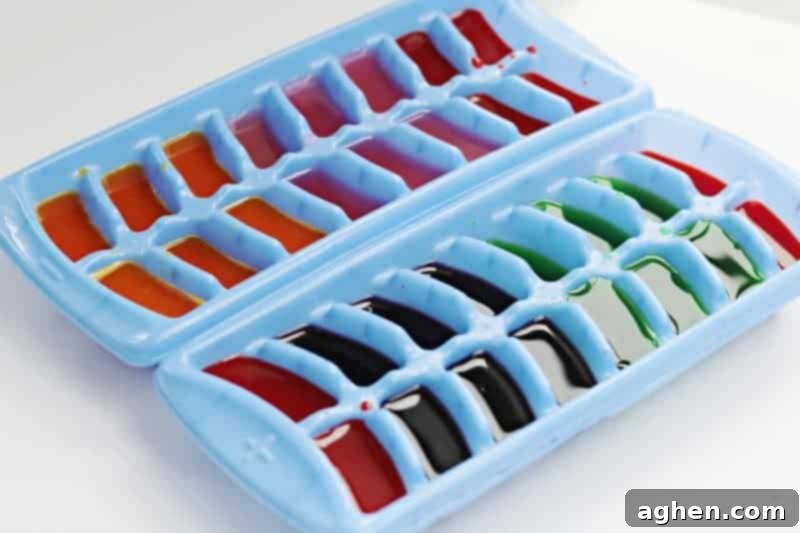 Hands filling an ice cube tray with different colored liquids made from drink mixes, preparing for a fun sensory activity.