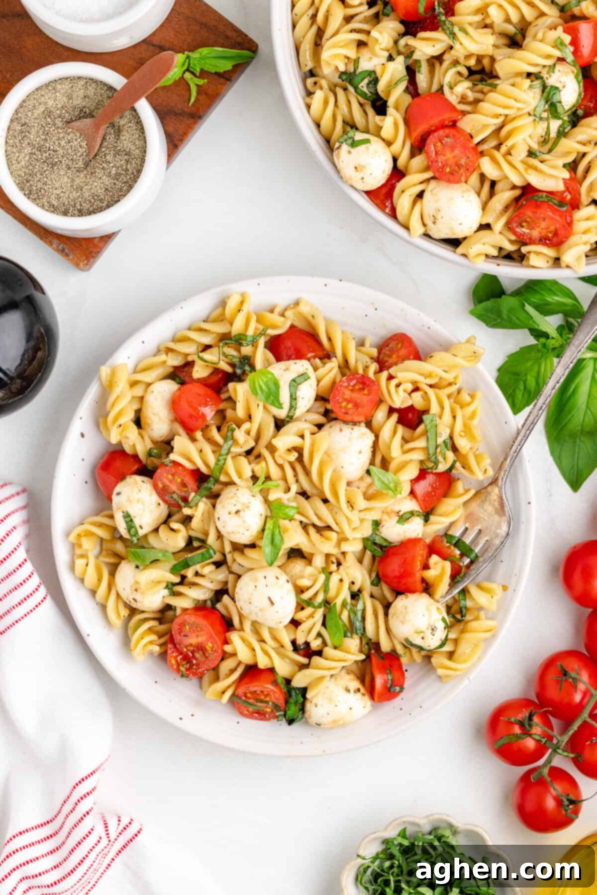 Bowl of rotini pasta salad with cherry tomatoes, mozzarella balls, and basil.