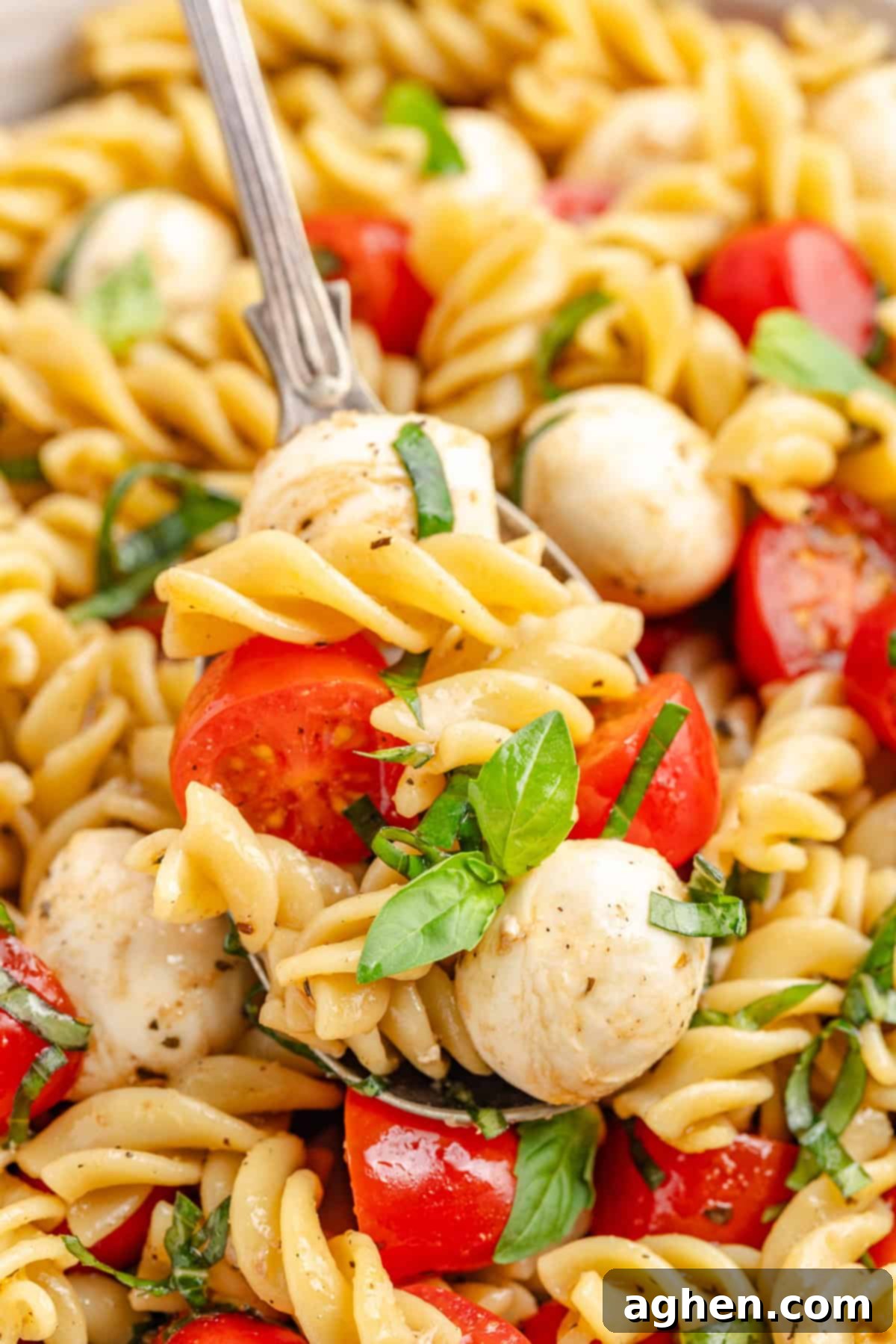 Close-up of a fork lifting a bite of caprese pasta salad with tomato, mozzarella, and basil.