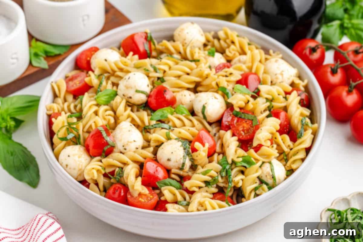 Bowl of pasta caprese salad with tomatoes and mozzarella, photographed from the side.