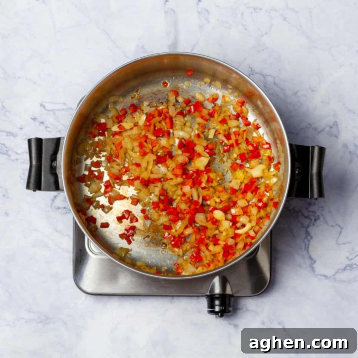 Onion and red bell pepper cooking on medium flame in a large pan