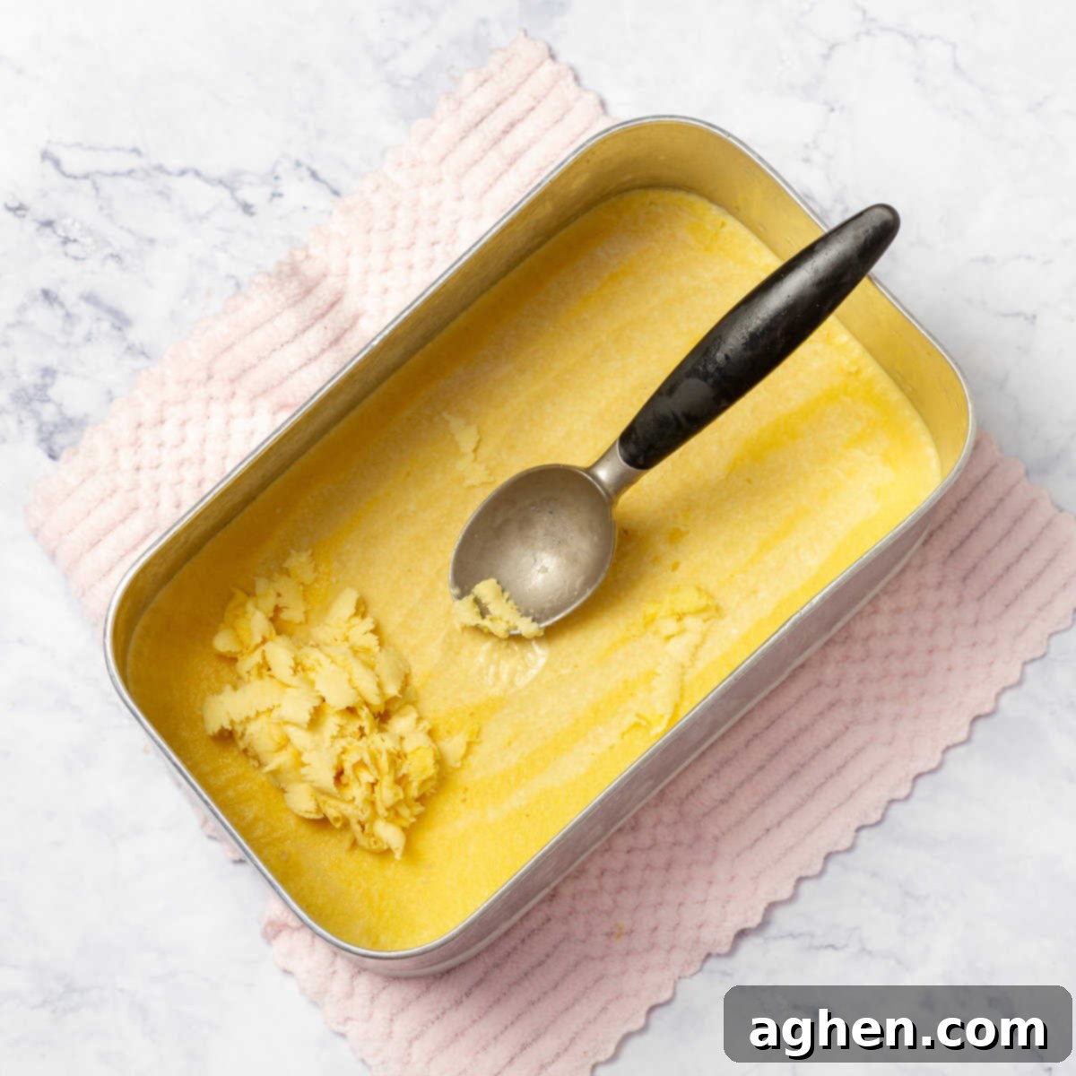 Tropical Mango Coconut Delight 6 Partially frozen Creamy Mango and Coconut Ice Cream mixture being scraped with a spoon to break up ice crystals.