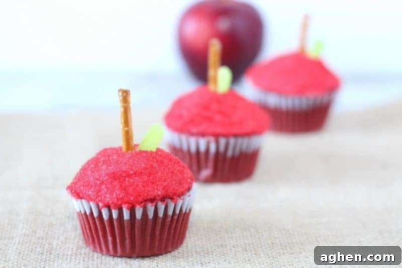 Bright red apple cupcakes with pretzel stems and green candy leaves, perfect for a back to school treat.