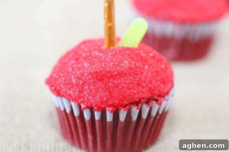 Delicious red velvet apple cupcakes topped with red sprinkles, pretzel stems, and green candy leaves.
