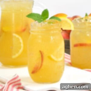 Sun Drenched Peach Lemonade 5 A mason jar of peach lemonade with lemon, peach slices, and mint, set in front of a pitcher and another jar.