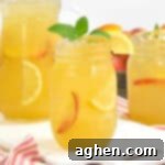 Sun Drenched Peach Lemonade 6 A mason jar of peach lemonade with lemon, peach slices, and mint, set in front of a pitcher and another jar.