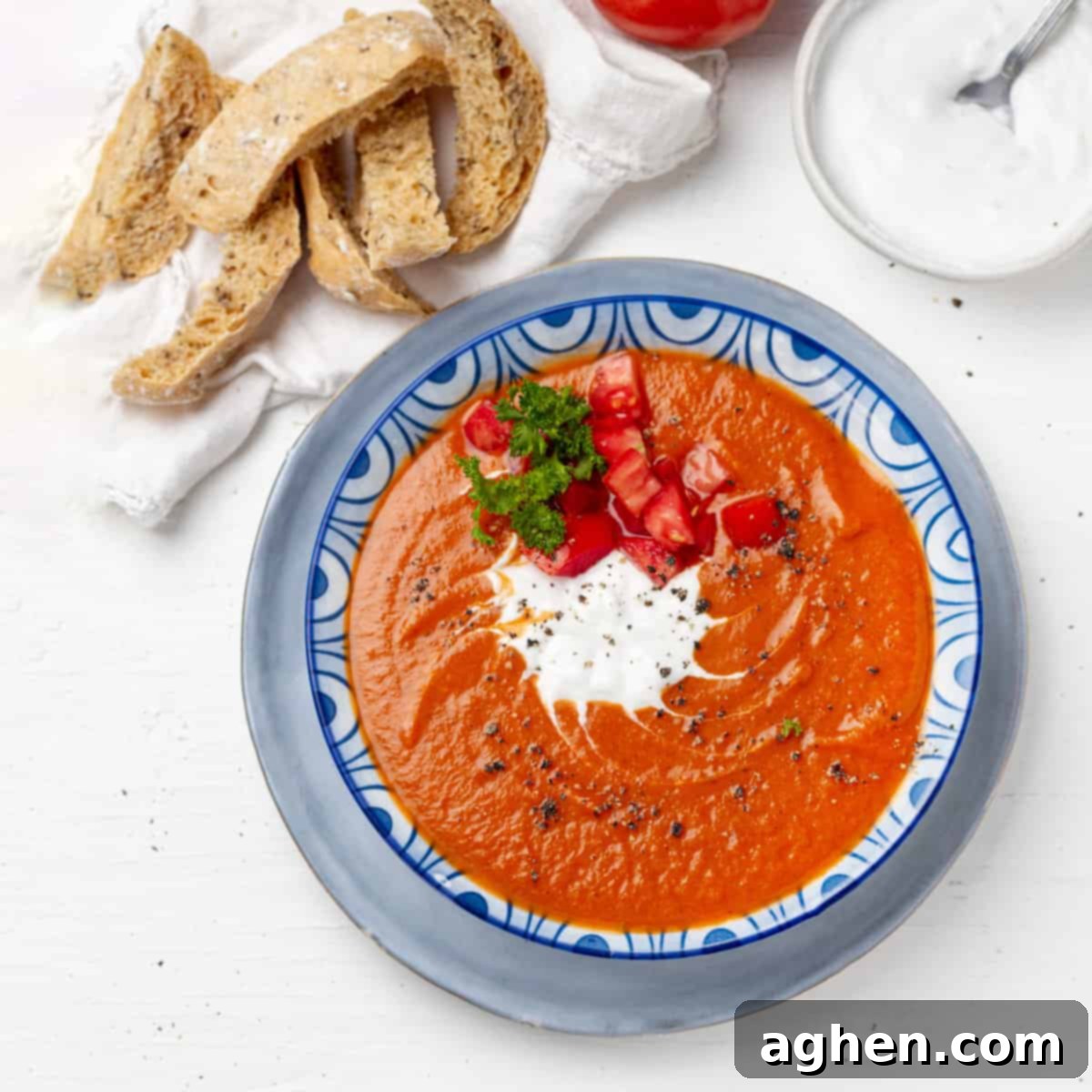 A steaming bowl of vibrant red tomato soup, garnished with fresh basil, served alongside ripe red tomatoes on a rustic wooden table, emphasizing freshness and comfort.