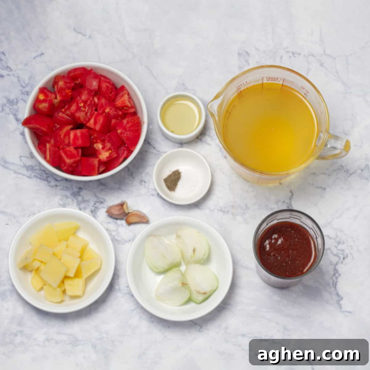 Essential ingredients for tomato soup displayed on a wooden board: fresh peeled and diced tomatoes, tomato juice, potato, onion, garlic, olive oil, and seasoning.