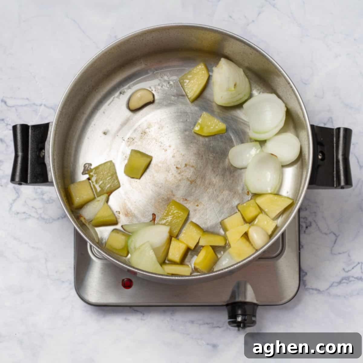 Chopped white onions and minced garlic are sautéing in olive oil in a stainless steel saucepan over medium heat, releasing fragrant aromas.