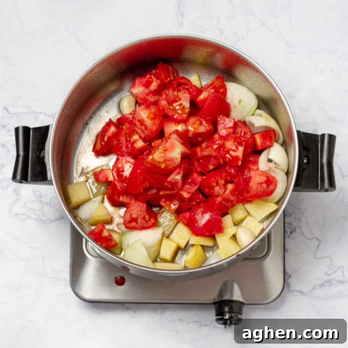 Diced tomatoes and peeled potato cubes are added to the sautéed onions and garlic in a saucepan, ready for stirring.