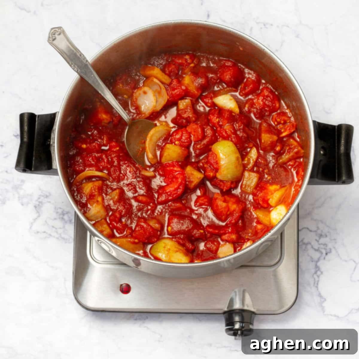 Chicken broth and tomato juice are poured over the simmering tomatoes and potatoes in a saucepan, ensuring they are fully covered.