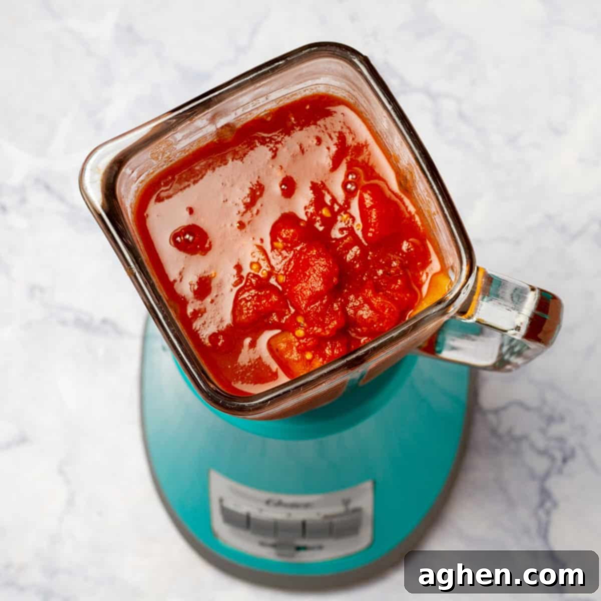 An immersion blender is actively blending the cooked tomato soup ingredients directly in the saucepan to achieve a smooth and creamy consistency.