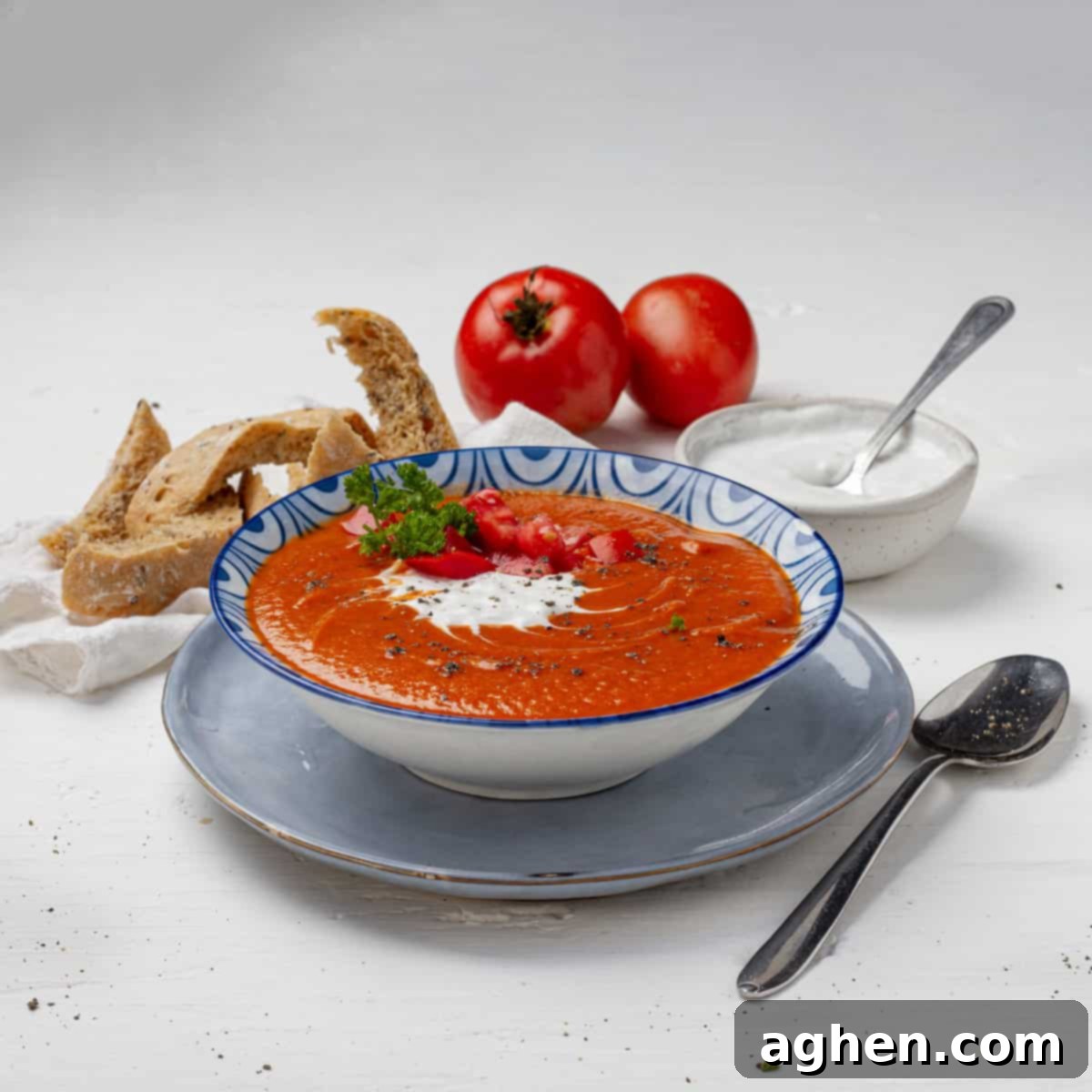 A warm bowl of homemade tomato soup, beautifully garnished with a swirl of Greek yogurt and fresh basil leaves, ready to be served.