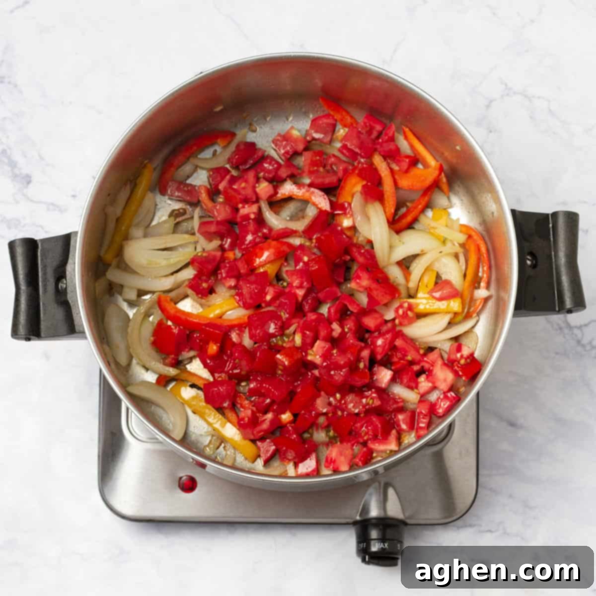 Sliced onions, red and yellow bell peppers, and diced tomatoes in a saucepan