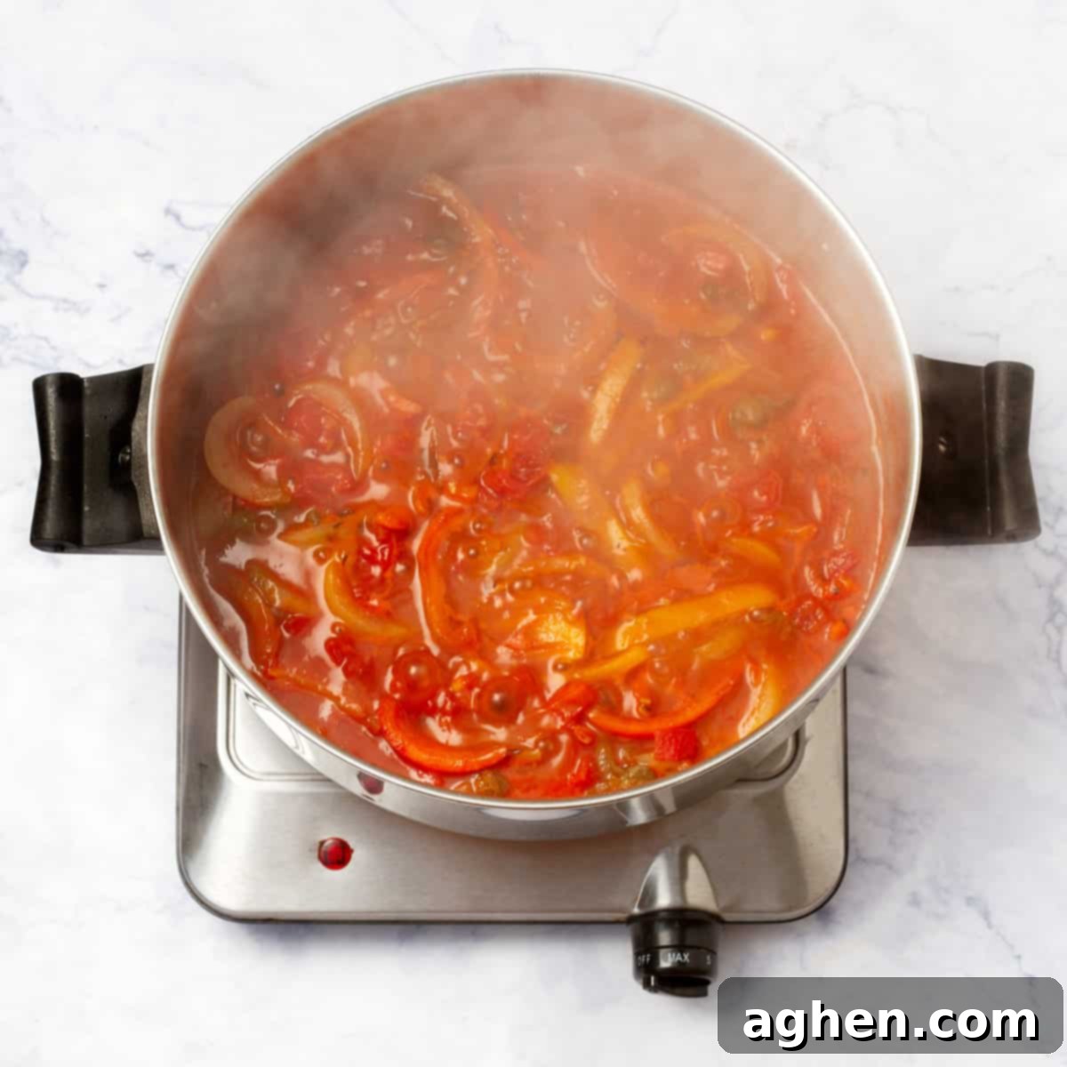 Sliced onions, red and yellow bell peppers, and diced tomatoes cooking in a saucepan