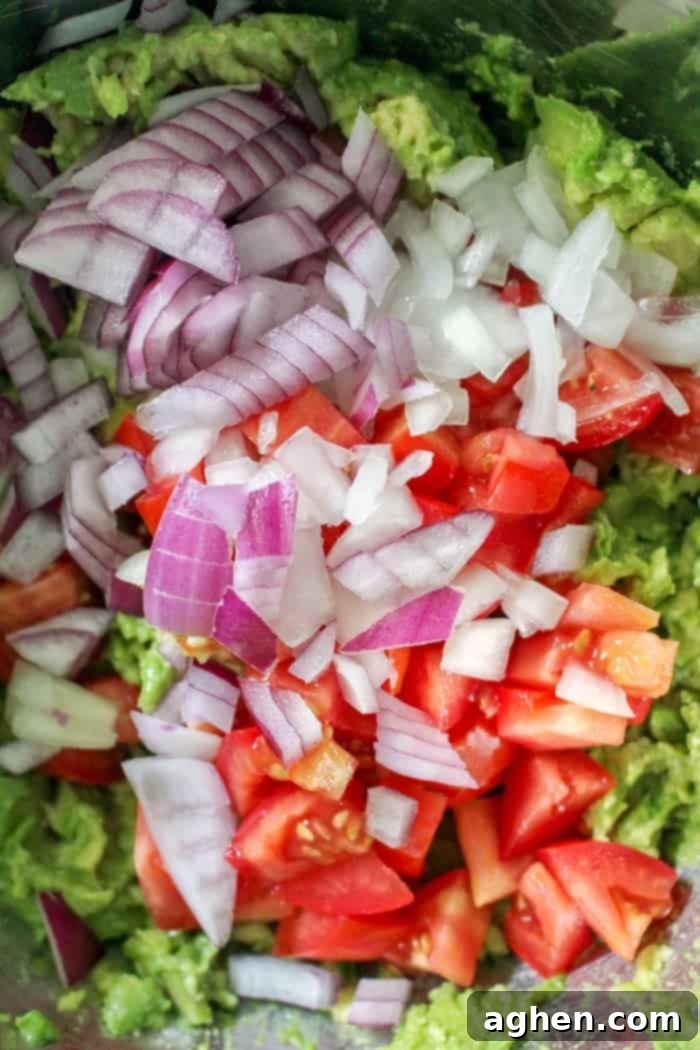 Fresh ingredients for a homemade guacamole recipe, showing diced tomatoes, onions, cilantro, and lime ready to be mixed with mashed avocado.
