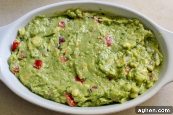 How to make guacamole: fresh ingredients being mixed together in a bowl, showing the process of combining mashed avocado with diced vegetables and lime juice.