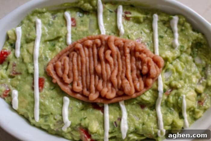 Piping refried beans onto guacamole to create the shape of a football, an easy game day guac in process.