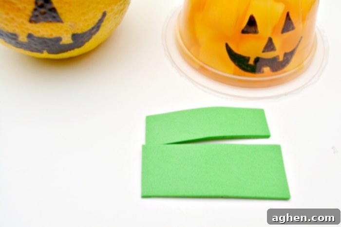 Step-by-step image demonstrating how to draw a jack-o-lantern face on a fruit cup and attach a green craft foam stem for Halloween.