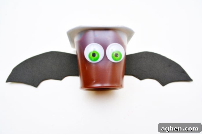 A completed chocolate pudding cup transformed into an adorable Halloween bat snack with googly eyes and black craft foam wings.