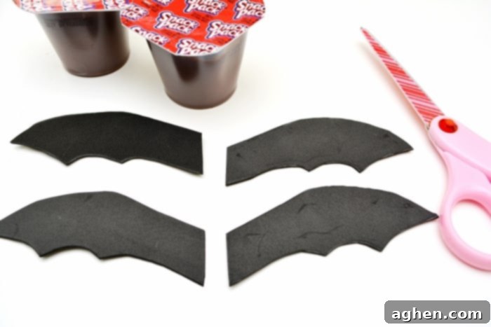 Step-by-step guide showing how to cut and attach black craft foam wings to a chocolate pudding cup to create a bat Halloween snack.