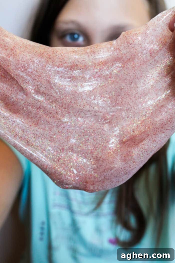 Young girl playfully stretching vibrant, glittery fall slime, highlighting the fun and tactile experience of homemade slime.