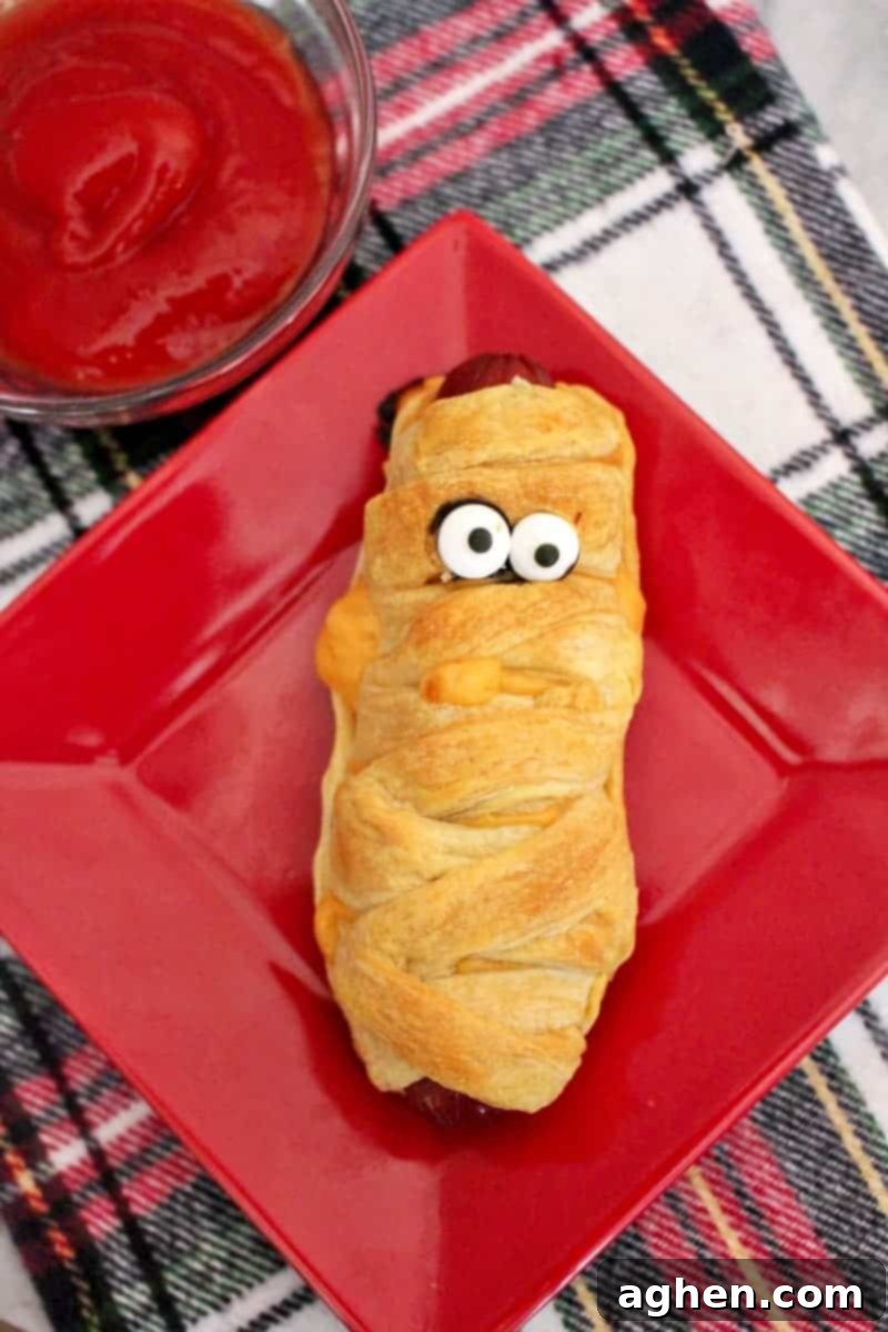 Close-up of baked crescent roll hot dog mummies arranged on a platter, ready for candy eyes and serving at a Halloween gathering.