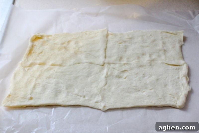 Crescent roll dough unrolled and flattened on a cutting board, ready to be cut into strips for mummy hot dogs.