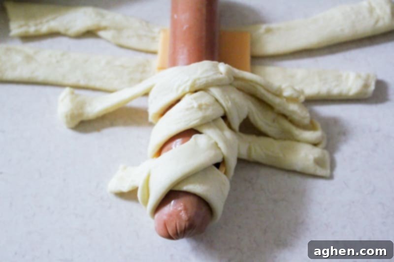 Step-by-step guide on how to wrap a hot dog with crescent roll dough to create the mummy effect.
