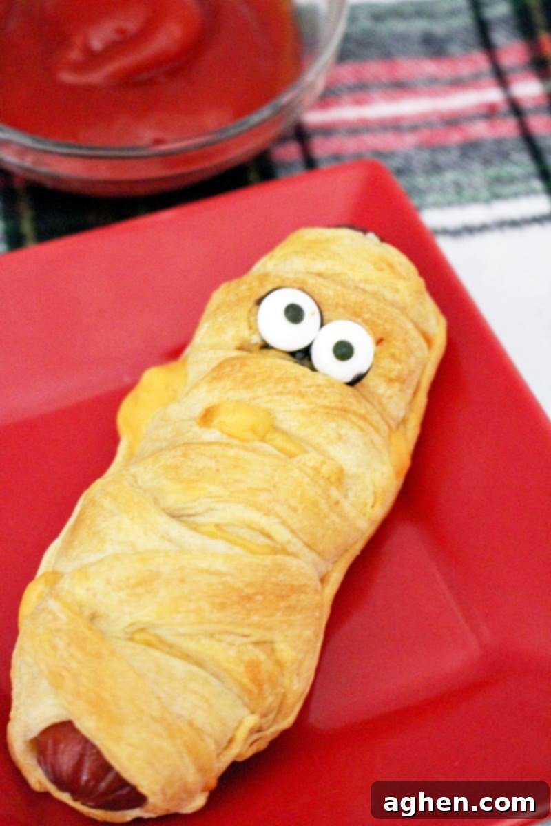 Finished mummy hot dogs with candy eyes, arranged on a plate and ready to be served as a fun Halloween dinner or party snack.